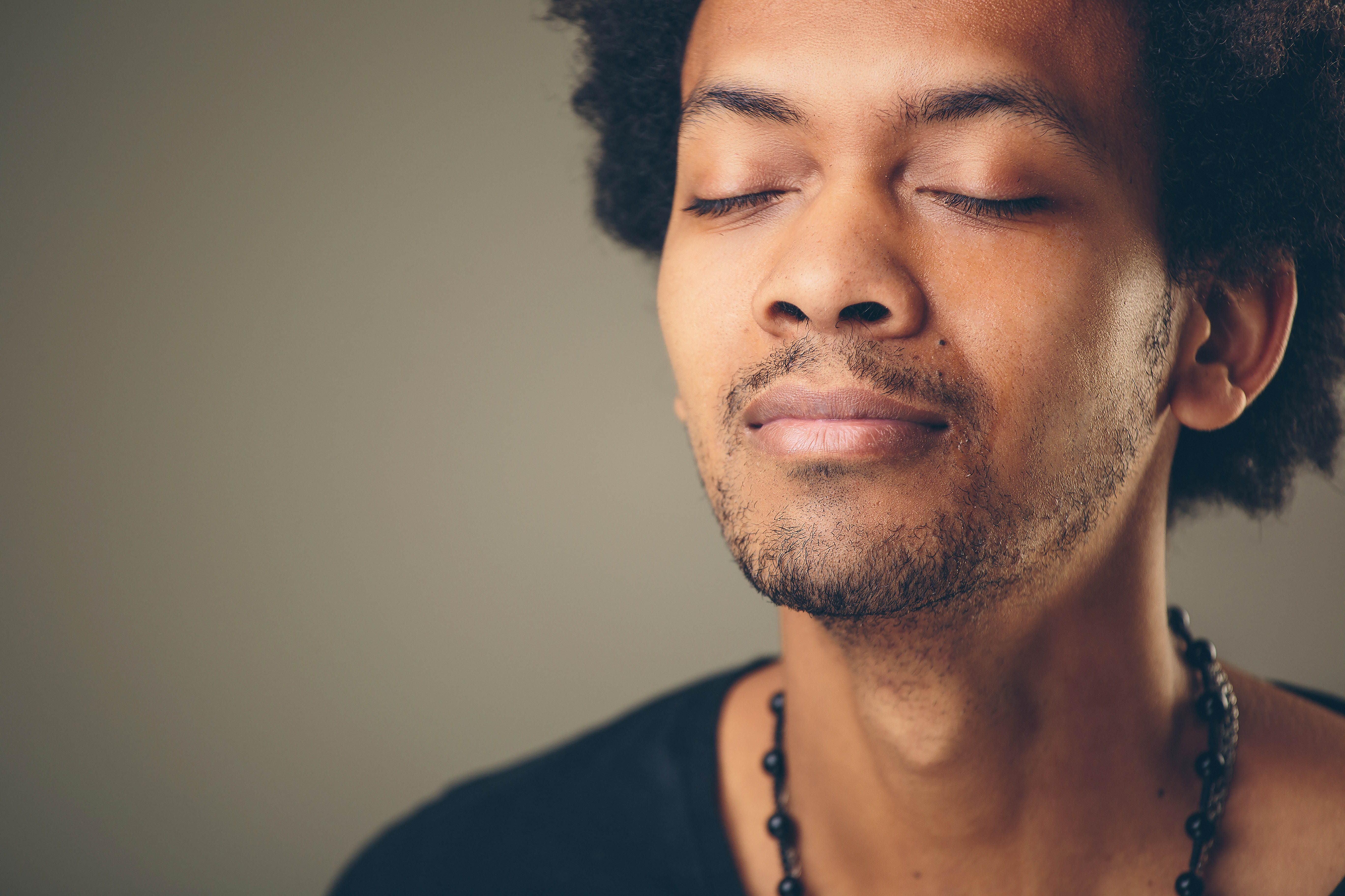 Close-up of young black man with his eyes closed, breathing in deeply. 